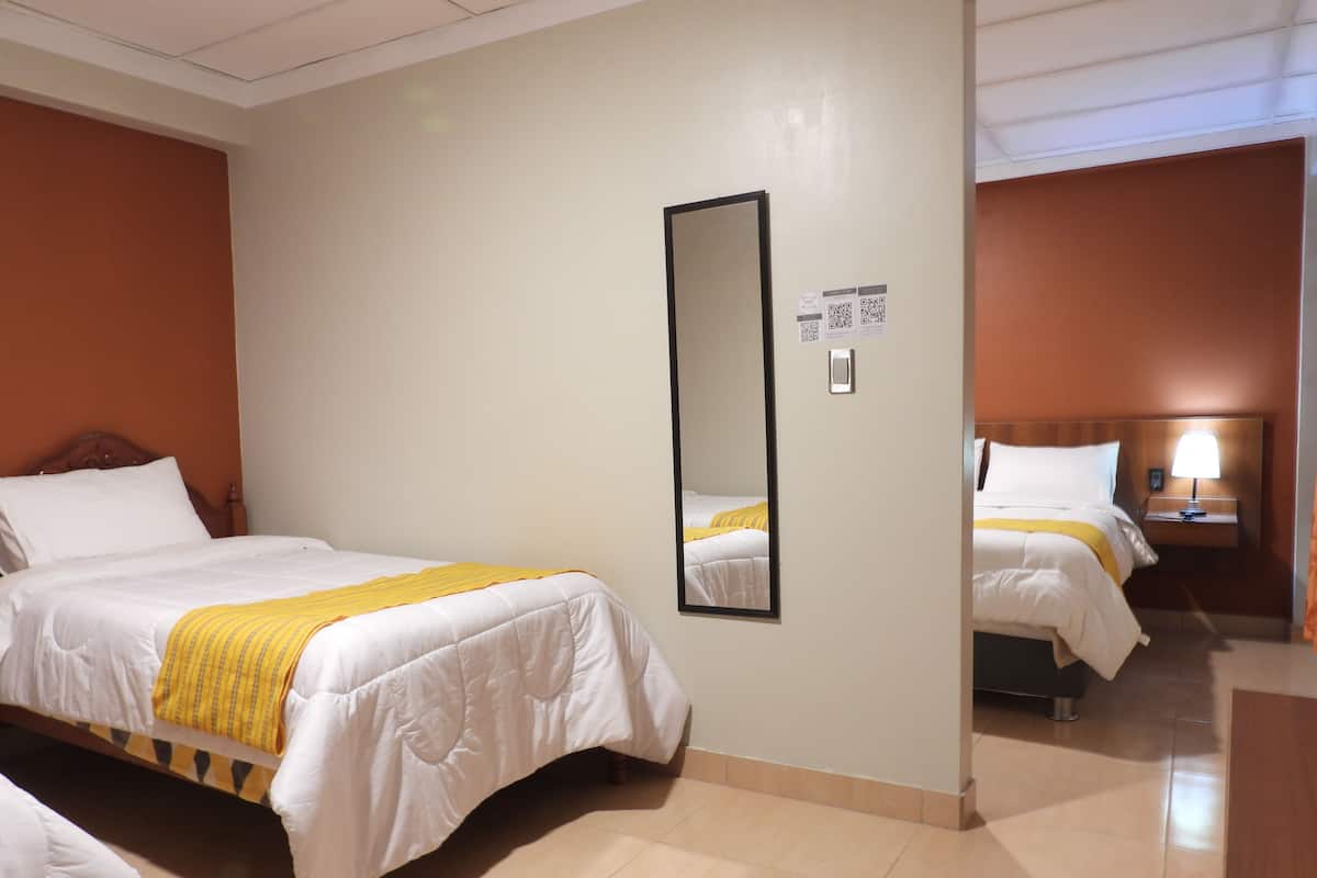 Une chambre d’hôtel avec deux lits, un miroir, une table de chevet avec une lampe et une tête de lit en bois.