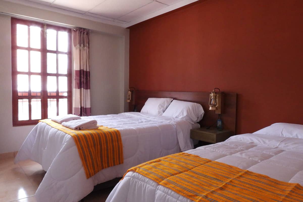 Une chambre d’hôtel avec deux lits, une fenêtre avec des rideaux et une table de chevet avec une lampe.