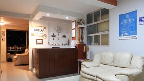 A hotel lobby with a reception desk, a clock, and a poster on the wall.