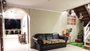 A spacious living room with a black leather sofa, a dining table with chairs, and a staircase leading to an upper level.