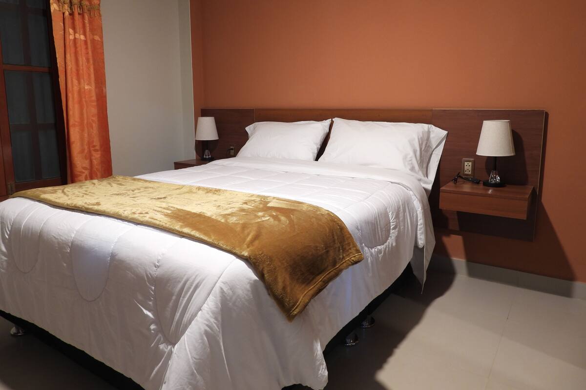 Une chambre d’hôtel avec un grand lit, deux tables de chevet avec des lampes et une fenêtre avec des rideaux.