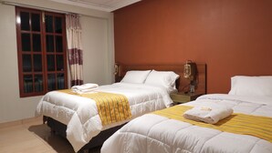 A hotel room with two beds, a window with curtains, a nightstand with a lamp, and a tiled floor.