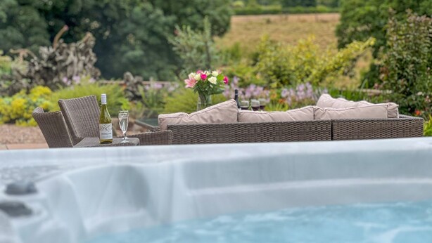 A hot tub with wicker furniture and a table set with wine glasses and a bottle. - High House, Southwaite -  a cottage that sleeps 10 guests  in 5 bedrooms (Southwaite)
