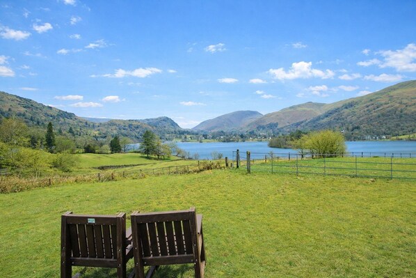 A bench in a grassy field with a lake and hills in the background.