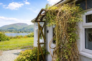 A rustic building with a window, a wooden structure attached to the wall, and a view of a lake and hills in the background.
