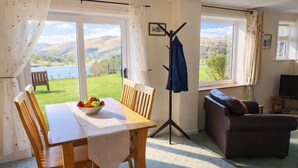 A room with a dining table, chairs, a bowl of fruit, a coat rack, a sofa, and a television.