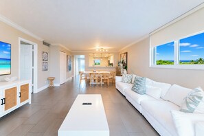 A spacious living room with a white sofa, a coffee table, and a TV on the left.