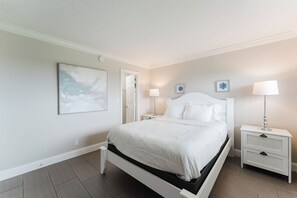 A bedroom with a bed, two bedside tables, a nightstand, and a wall-mounted lamp.