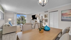 A modern living room with a wooden dining table, a sofa, and a coffee table. There is a chandelier above the table and a painting on the wall. - Lux 2 Bedroom - 2 Bathroom w/Balcony Directly Across from the Beach - Boca Raton (Boca Raton)