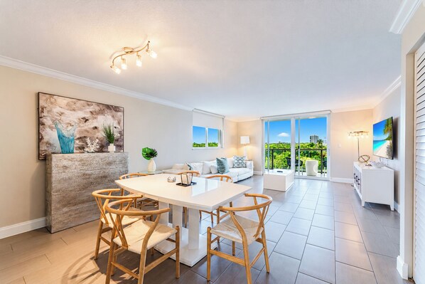 A modern interior with a dining area, a sofa set, and a view of the outdoors.