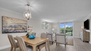 A modern dining area with a wooden table, chairs, and a blue vase centerpiece. There is a painting on the wall and a view of greenery outside. - Lux 2 Bedroom - 2 Bathroom w/Balcony Directly Across from the Beach - Boca Raton (Boca Raton)
