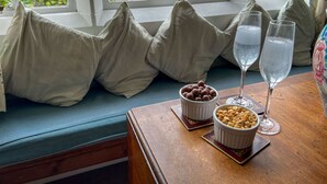 Uitzicht vanuit een raam met een bankje, kussens, een schaal met chocoladeballetjes, een schaal met pinda's en twee glaasjes water.