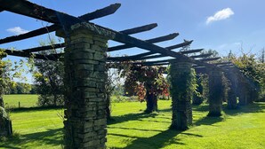 Een pergola van steen in een gazon, met een heldere lucht.