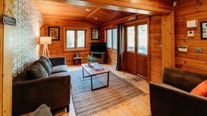 Ein gemütliches Blockhaus-Interieur mit einer Couch, einem Sessel und einem Fernseher auf einem Beistelltisch.