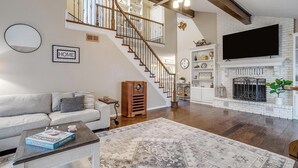 Un salón espacioso con una escalera, una chimenea y un televisor de pantalla plana montado encima.