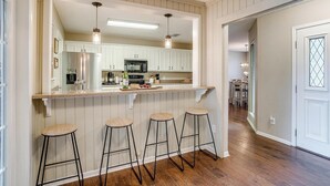 Una cocina con armarios blancos, encimera de madera y tres taburetes de bar.