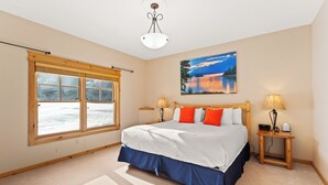 Un dormitorio con una cama grande, dos lámparas de noche, una ventana con persianas, un cuadro en la pared y una lámpara de techo.