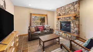Una sala de estar acogedora con chimenea de piedra, un ventanal grande y un televisor de pantalla plana.