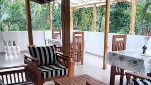 A wooden outdoor seating area with tables and chairs, a covered section with a table and chairs, and a view of greenery in the background. - Sanduhan Villa, Stay in Sri Lanka! (Warakapola)