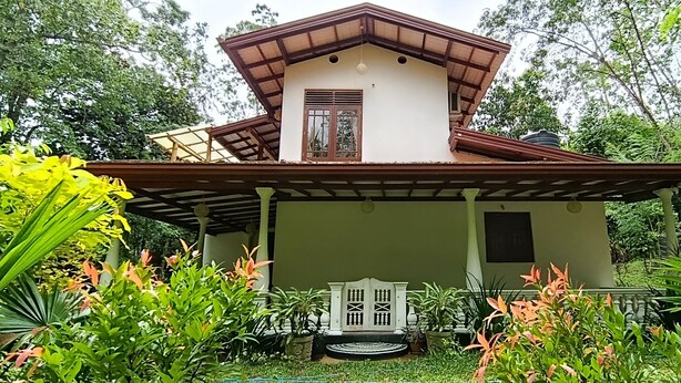 A two-story house with a covered porch, surrounded by lush greenery and tropical plants. - Sanduhan Villa, Stay in Sri Lanka! (Warakapola)