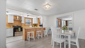 Una cocina moderna con detalles de madera, una isla central con taburetes y una zona de comedor con sillas blancas.