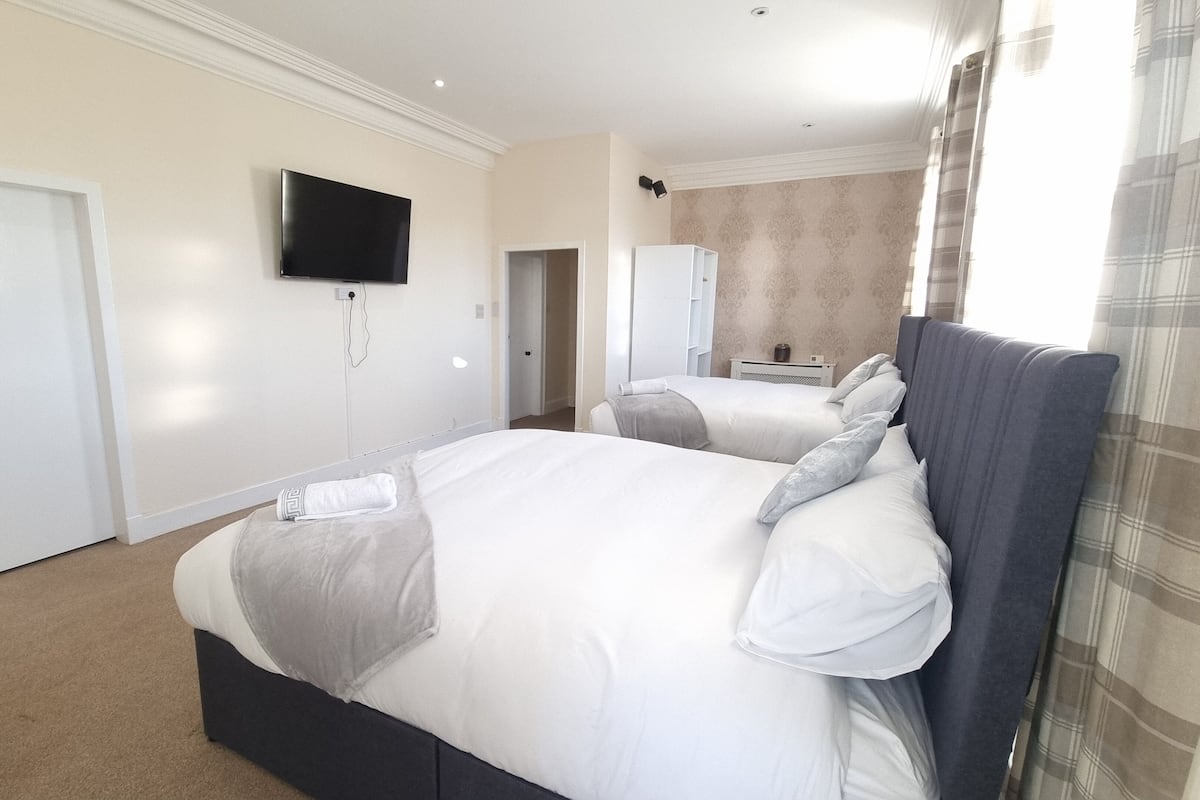 A hotel room with two beds, a TV mounted on the wall, and a bathroom visible through an open door.