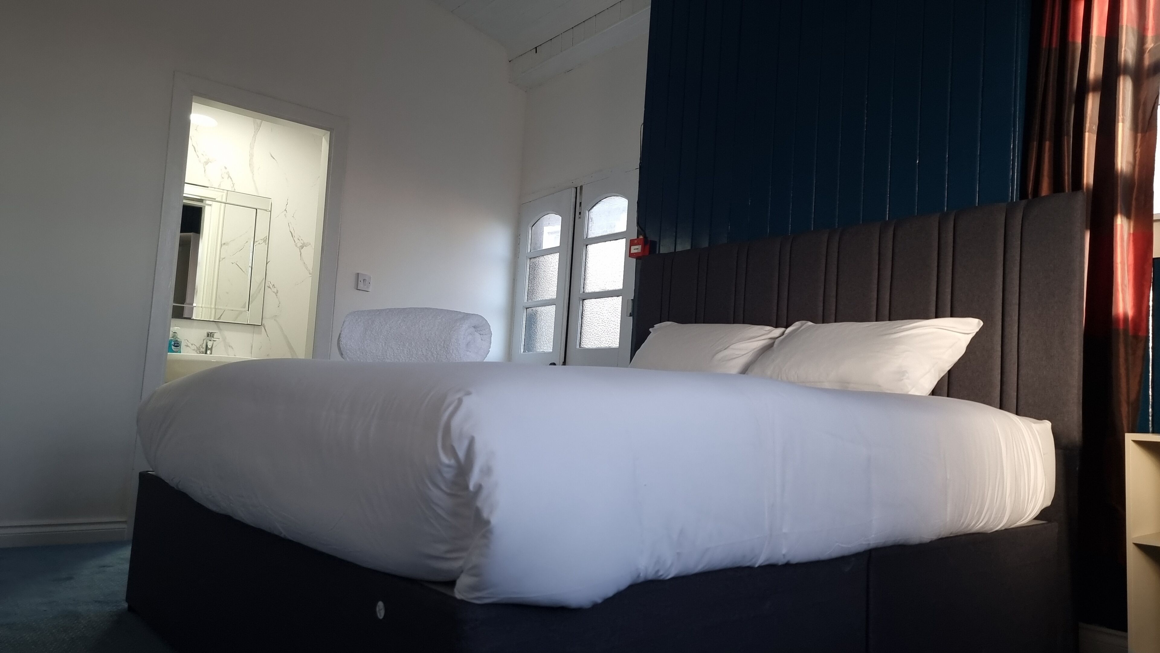 A bedroom with a large bed, a window, a door, and a mirror.