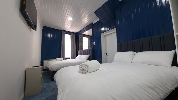 A hotel room with two beds, a large window with curtains, a radiator, and a door. - Ye Olde Hotel (St. Andrews)