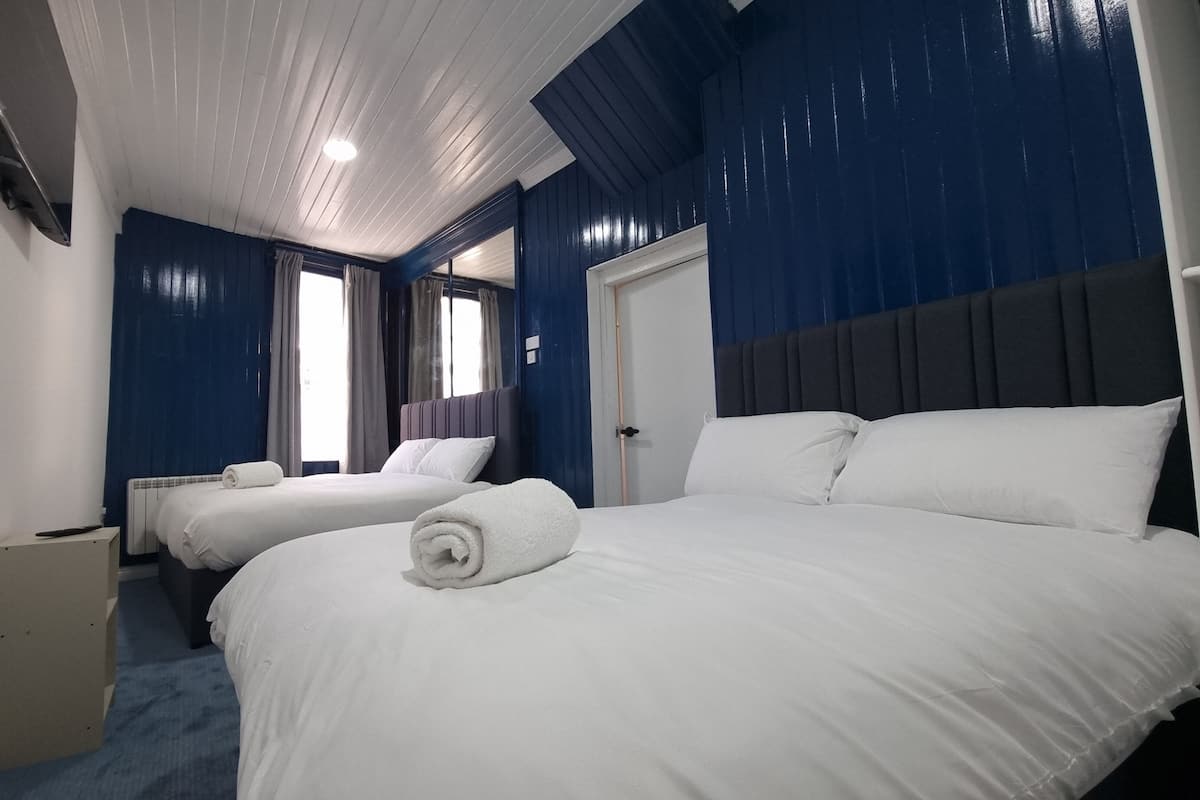 A hotel room with two beds, a large window with curtains, a radiator, and a door.