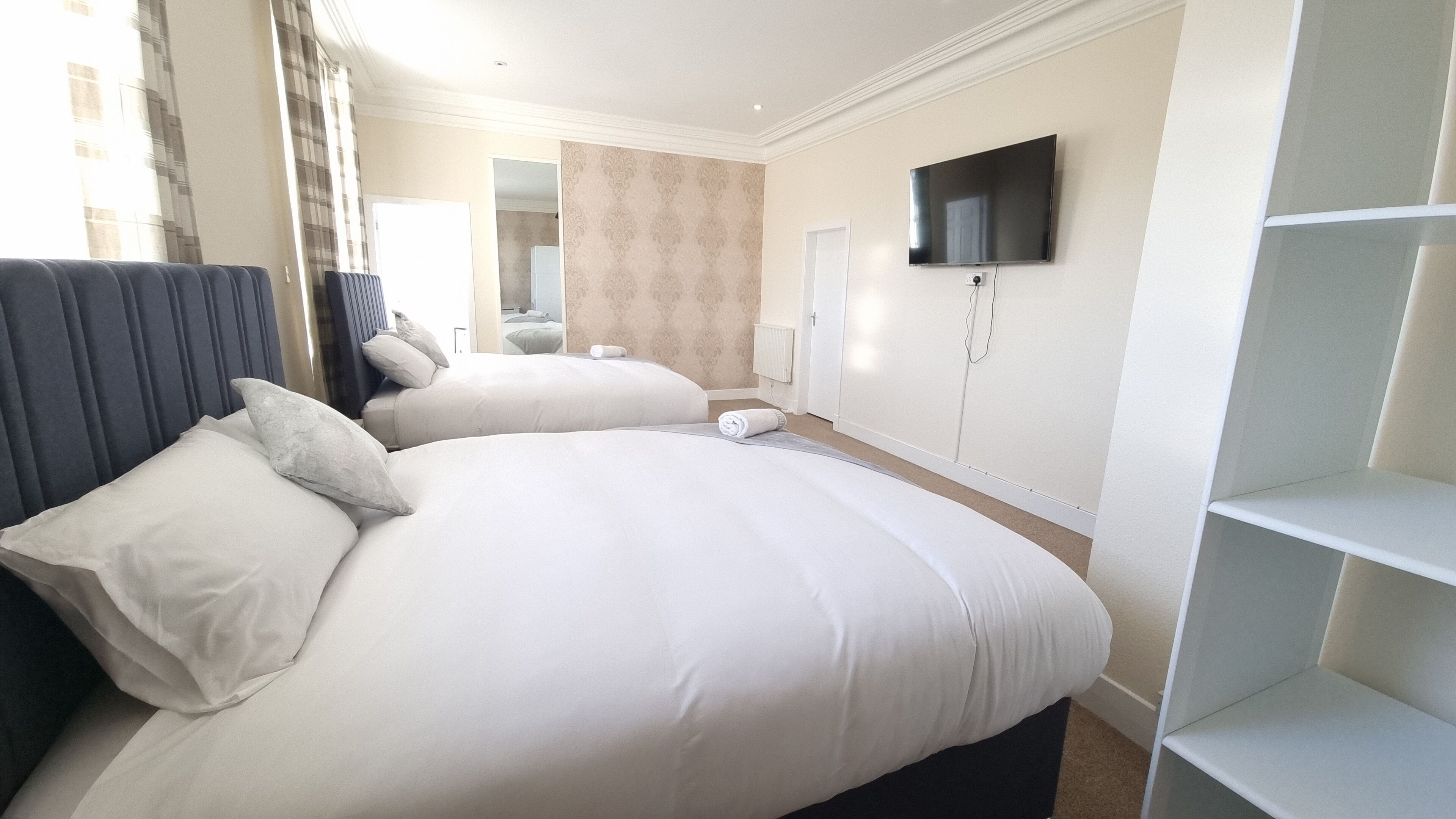 Habitación de hotel con dos camas, un televisor en la pared y un ventanal con cortinas.