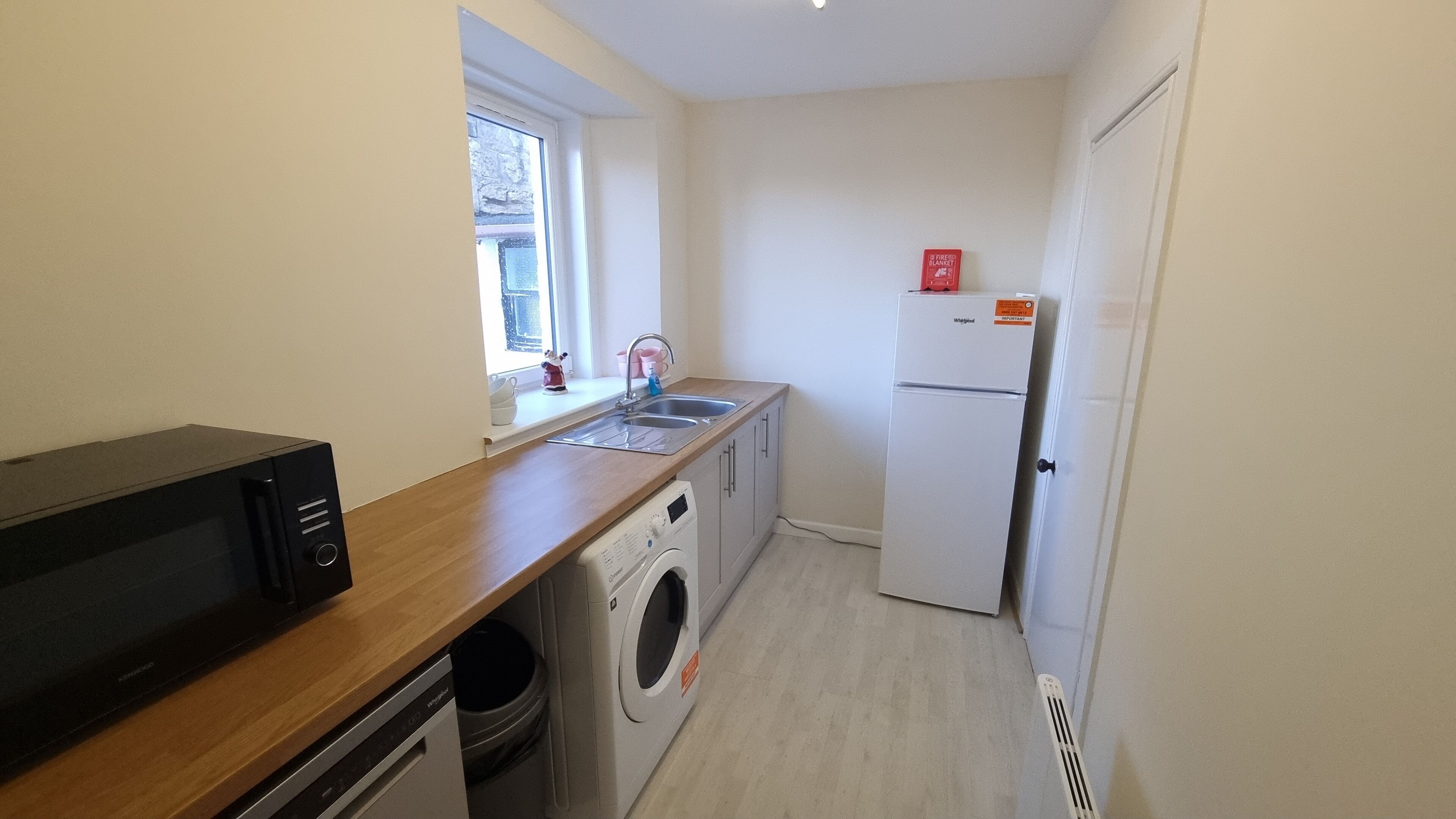 A compact kitchen with a washing machine, a refrigerator, and a window providing natural light.