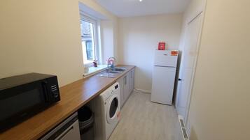 A compact kitchen with a washing machine, a refrigerator, and a window providing natural light.