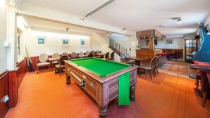 A pool table in a room with multiple chairs and tables, a bar area, and a staircase leading to another level. - Ye Olde Hotel (St. Andrews)