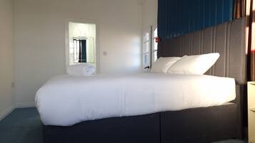 Una cama bien tendida con sábanas blancas en una habitación con cabecera oscura y una ventana con cortinas.