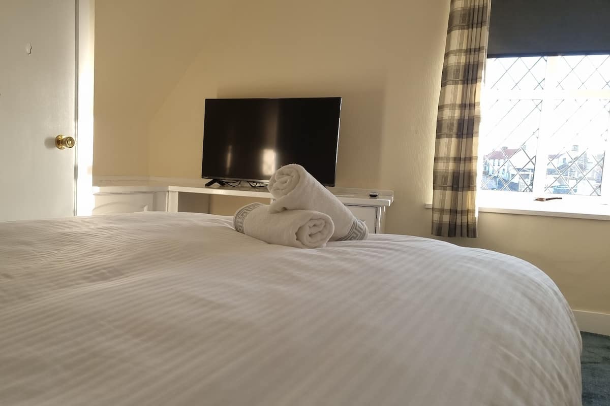 A hotel room with a large bed, a television on a stand, and a window with curtains.