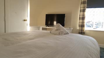 Een hotelkamer met een groot bed, een televisie op een standaard en een raam met gordijnen.
