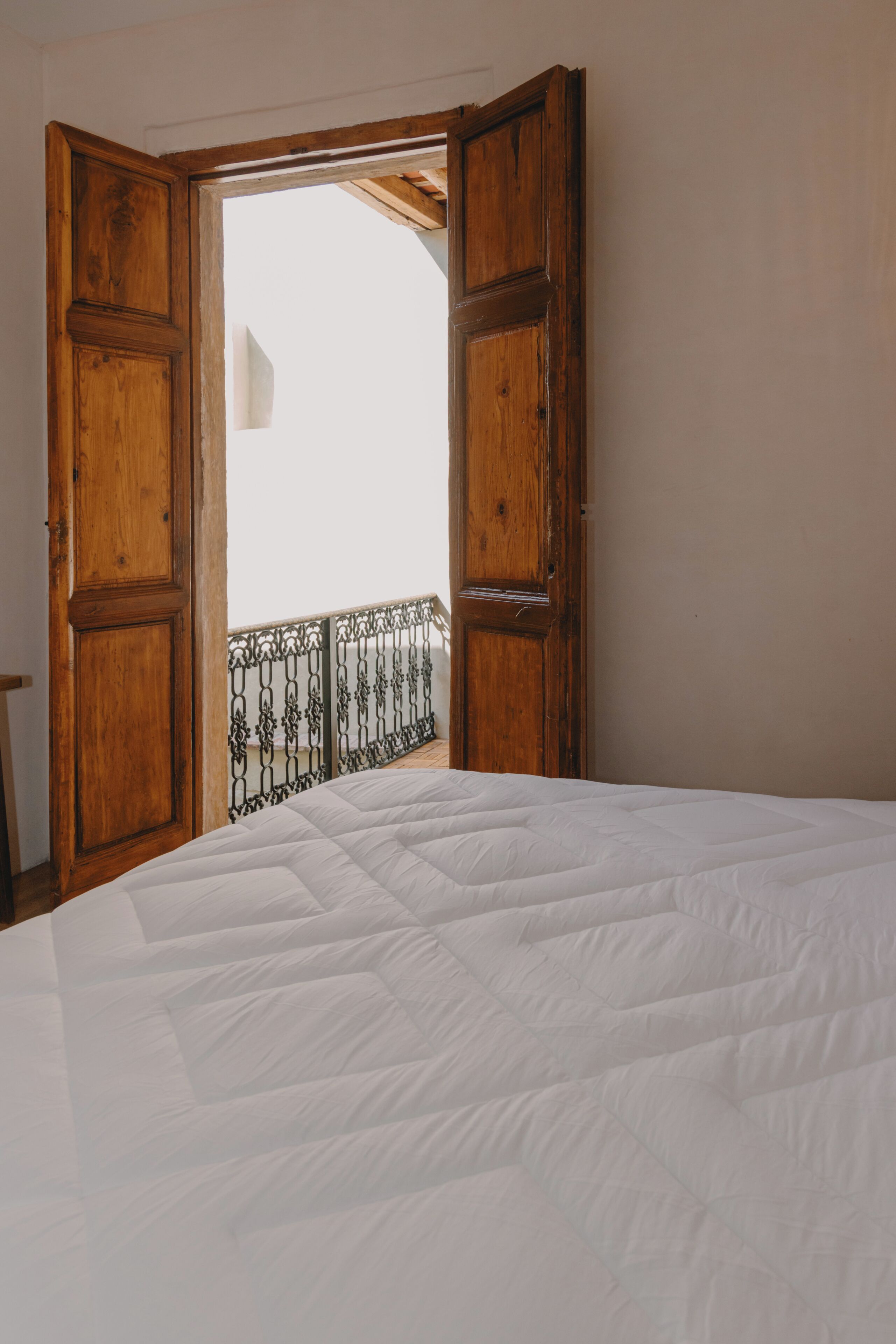 A room with a bed, a wooden door, and a balcony with a metal railing.