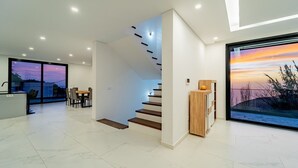 Een modern interieur met een trap, een eetgedeelte en een groot raam met uitzicht op een zonsondergang.