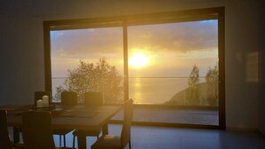 Een eethoek met een groot raam met uitzicht op een zonsondergang boven het water.