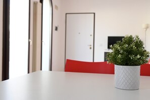 A room with a white table, a red chair, a white textured pot with green foliage, and a closed door in the background. - P045 – Porto Recanati, splendid three-room apartment 300 meters from the sea (Porto Recanati)