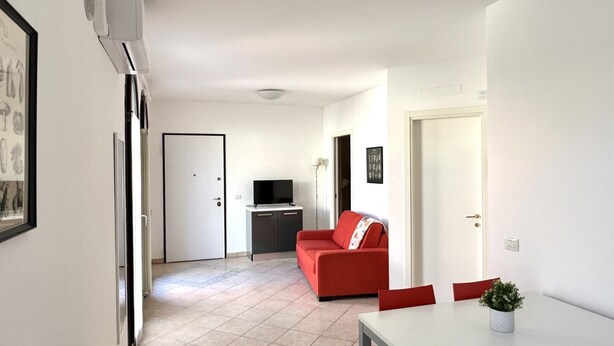 Un espacio habitable compacto con kitchenette, un sofá rojo, una mesa de comedor y un televisor.