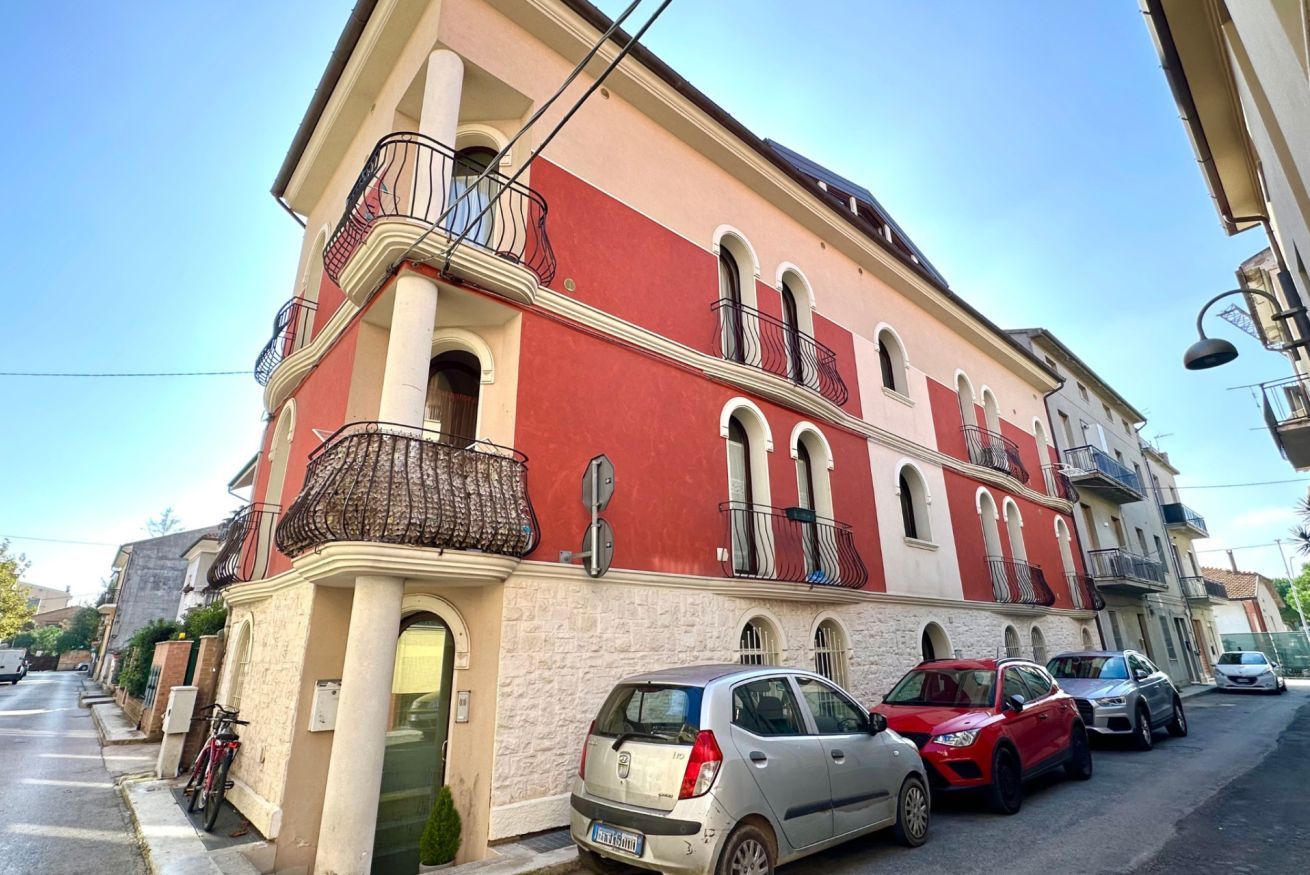 A multi-story building with balconies, parked cars, and a clear sky.