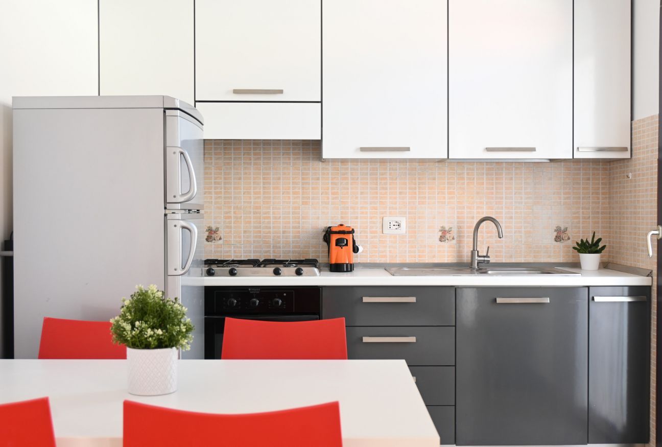 A modern kitchen with white cabinets, a stainless steel refrigerator, a gas stove, and a sink.