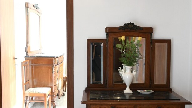 Una cassettiera in legno con uno specchio, un vaso con fiori e un piatto.