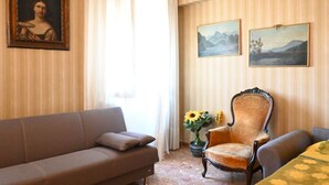 Una stanza con un divano, una poltrona, un quadro e un vaso con fiori.