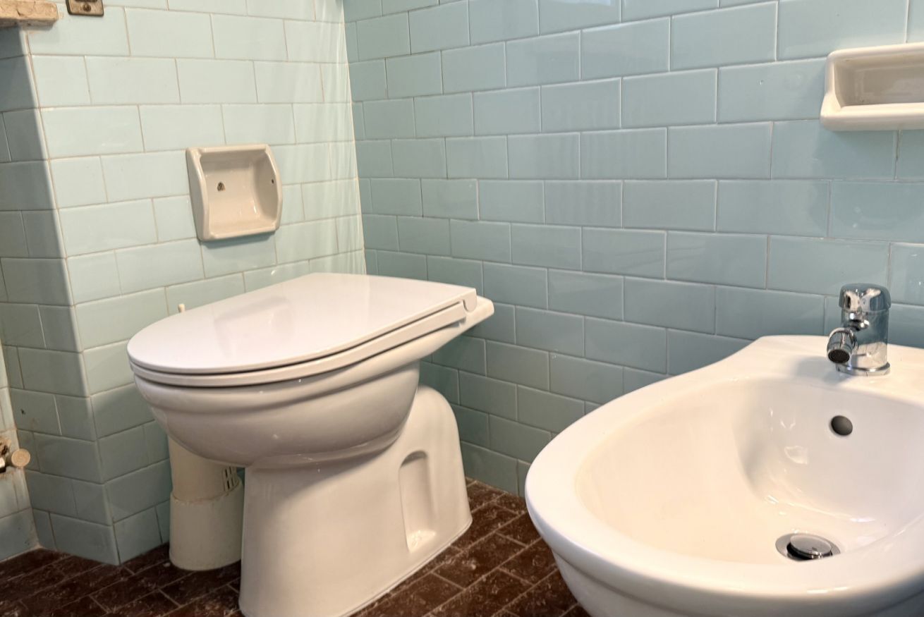 Een badkamer met een toilet, een wastafel en een zeepdispenser aan de muur.