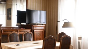 Zona pranzo con tavolo, sedie, televisore e lampada.