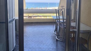 Un balcone con vista sulla spiaggia e sull'oceano, con sedie in metallo e un tavolo.