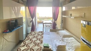 Una stanza compatta con un letto, una televisione, un tavolino e una finestra con tende.