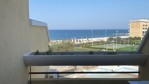 Un balcone con vista sul mare, edifici e un campo sportivo.